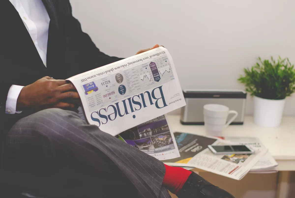 A person sitting near a table holding a newspaper
